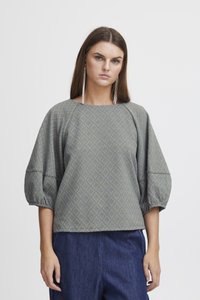 Blouse gris-bleu à motifs avec un design en losange, manches larges et coupe carrée, associée à un pantalon en denim foncé.