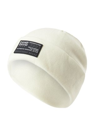 White ribbed beanie hat featuring a black rectangular fabric label with text and coordinates. The texture is soft and knitted.