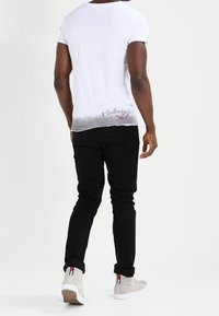 Hvid T-shirt med en ombre-fade til grå, der har teksten "Midnight Soul" ved kanten. Kombineret med sorte jeans og grå højhælede sneakers.