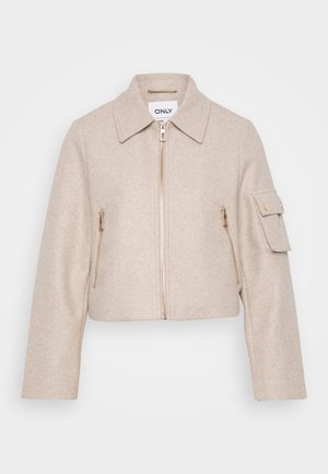 Giacca beige corta con colletto, chiusura frontale a zip e due tasche con zip. Il tessuto ha una consistenza morbida; presenta dettagli in hardware dorato.