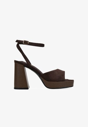 Braune Wildleder-Plateausandalen mit geschlossenem Zeh, breitem Knöchelriemen und einem strukturierten Blockabsatz mit horizontalen Linien.