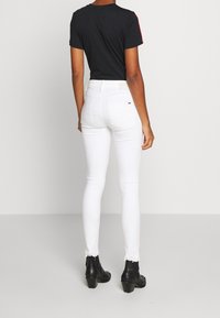 Jeans blancos ajustados con un dobladillo deshilachado, combinados con una camiseta negra. Los jeans tienen bolsillos traseros y una pequeña etiqueta de marca en la cinturilla.