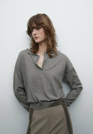 Gray, long-sleeved henley top with a placket and buttons. Soft texture and relaxed fit, paired with a beige, high-waisted skirt featuring side accents.