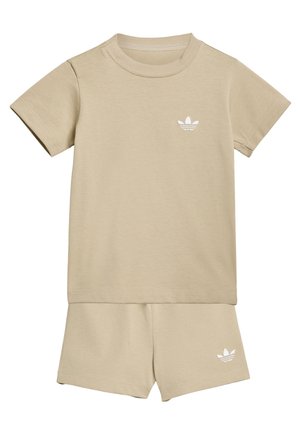 Beige sæt med T-shirt med korte ærmer og shorts med hvide Adidas trefoil-logoer på brystet og venstre ben.