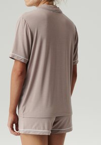 Beżowy komplet piżamy z krótkim rękawem wykonany z bawełny, z białymi lamówkami. Bluzka ma kołnierzyk, a szorty mają luźny krój i wykończone są mankietami.
