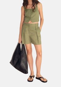 Top corto verde oliva e pantaloni corti abbinati, entrambi in tessuto leggero. Accessoriato con una borsa a tracolla nera intrecciata e ciabatte nere.