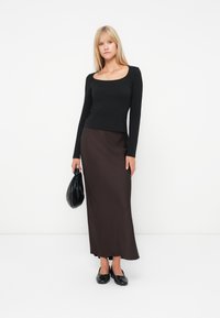 Haut noir à manches longues avec un décolleté carré associé à une longue jupe marron, complété par un sac à main noir et des chaussures plates noires.