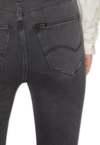 Jeans de mezclilla gris oscuro con un diseño ajustado, que cuentan con dos bolsillos traseros y una etiqueta de la marca Lee en el bolsillo derecho. Textura suave, con un diseño minimalista.