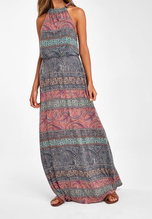 Femme portant une robe longue sans manches à col licou avec des rayures horizontales multicolores à motifs paisley et floraux, associée à des sandales marron.