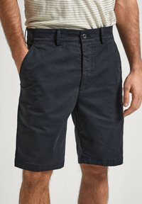 Pantalones cortos de algodón azul marino oscuro con frente plano, bolsillos laterales y puños rematados, con cierre de botón y pasadores para cinturón.