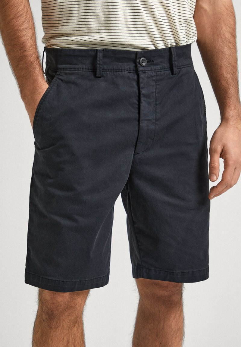 Pantalones cortos de algodón azul marino oscuro con frente plano, bolsillos laterales y puños rematados, con cierre de botón y pasadores para cinturón.