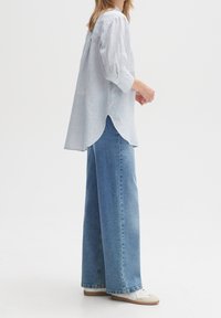 Ljusblå rutig skjorta med trekvartsärmar, bakveck, tillsammans med högmidjade vida blå jeans och vita sneakers.