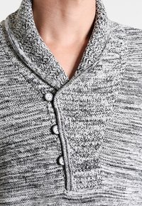 Sweter z dzianiny z kołnierzem w kolorze szarym z teksturowanym wzorem; posiada trzy guziki przy szyi i kontrastową lamówkę wokół kołnierza.