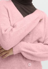 Ljusrosa stickad cardigan gjord av ett mjukt, texturerat tyg med V-hals, långa ärmar och två matchande knappar fram.