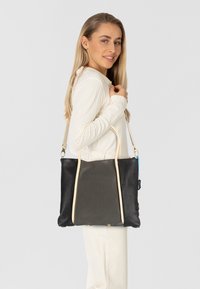 Zwarte leren tote bag met lichtbeige handvatten en metalen accenten. Rechthoekige vorm met een gestructureerd oppervlak en zijzakken.