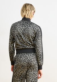 Giacca di tuta con stampa leopardata, dotata di polsini e colletto a coste neri. Tessuto liscio e leggero con un design aderente e dettagli neri a contrasto.