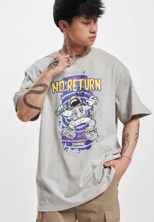 Lys grå grafisk t-shirt med et astronautdesign i lilla, gul og sort. Kortærmet og afslappet pasform med synlige tatoveringer.