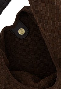 Brun ruskind taske indvendigt med en vævet tekstur; har et sort læderdetalje og messing trykknap.