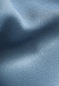 Tessuto azzurro chiaro con superficie leggermente strutturata, che mostra un motivo di tessitura fine e una qualità di caduta morbida, indicativa di un tessuto leggero.