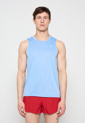 Jeune homme debout, face à l'avant, portant un débardeur bleu clair et un short de course rouge sur un fond uni.