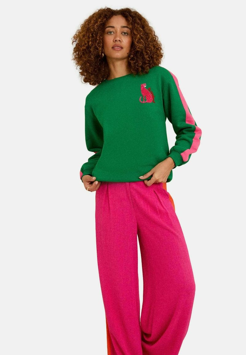 Felpa verde con strisce rosa, caratterizzata da un design di un gatto. Abbinata a pantaloni rosa larghi, in tessuto testurizzato e dalla vestibilità rilassata.
