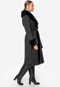 Dlouhý černý kabát vyrobený z měkké tkaniny, s velkým límcem a manžetami z umělé kožešiny. S páskem, hladkou texturou a strukturovanou siluetou.