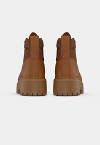 Bottines en cuir marron avec une semelle en caoutchouc robuste, un talon texturé et des détails cousus sur les côtés, ornées d'accents dorés.