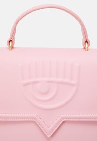 Růžová kožená taška s pevným designem, raženým motivem oka, horním uchycením a akcenty v pozlaceném tónu. Hladká textura a čisté linie.