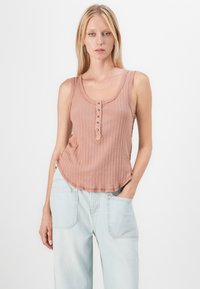 Zandroze geribbelde tanktop met een ronde hals, knopenlijst en een relaxte fit, gecombineerd met lichtblauwe wijde jeans.