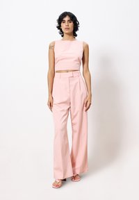 Rosa, verkürztes Oberteil mit Rundhalsausschnitt, kombiniert mit hochtaillierten, weiten Hosen aus passendem rosafarbenem Stoff und flachen rosa Sandalen.