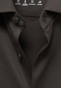 Polo de color marrón oscuro con una tela texturizada, dos botones y un diseño de cuello clásico. Presenta características sin plancha y termorreguladoras.