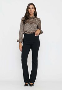 Blusa a stampa leopardata con design a bottoni, abbinata a pantaloni neri aderenti e scarpe nere a punta. Tessuti lisci e vestibilità su misura.