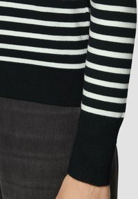 Gestreifter Pullover in Schwarz und Weiß mit einem gerippten Bündchen. Das Material wirkt weich und gestrickt, mit einem taillierten Design, das bis zum Handgelenk reicht.
