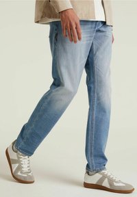 Jeans de mezclilla azul claro con un corte recto, combinados con zapatillas blancas y grises que tienen una suela texturizada y acentos en contraste.