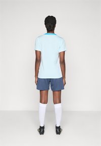Light blue short-sleeve sports shirt with a turquoise collar, paired with dark blue shorts, white socks, and black cleats.
