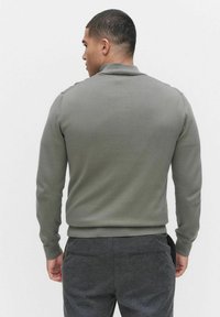 Szary sweter z długim rękawem, z ściągaczem na dole i przy mankietach, z kołnierzem typu mock oraz delikatnymi akcentami na ramionach, zestawiony z ciemnoszarymi spodniami.