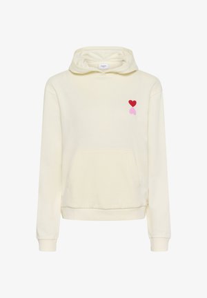 Hanorac cu glugă, de culoare crem, cu buzunar frontal și modele mici de inimioare roșii și roz pe partea stângă a pieptului.