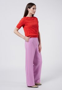 Suéter corto rojo de manga corta con patrón texturizado, combinado con pantalones de pierna ancha de talle alto en color lavanda y zapatos de color dorado.
