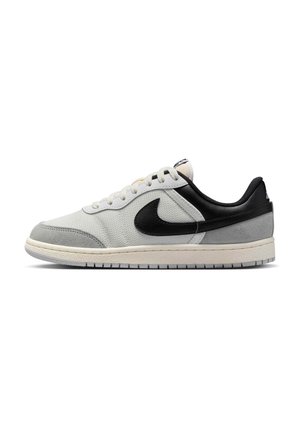 Baskets basses blanches et grises avec talon noir et logo Nike, lacets blancs et semelle texturée, vues de profil.