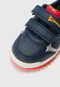 Baskets pour enfants en cuir bleu avec des bandes Velcro, semelle en caoutchouc rouge, embout perforé pour la respirabilité et accents de marque.