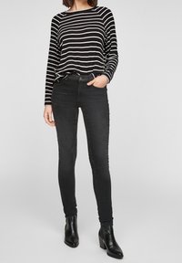 Schwarze eng anliegende Jeans kombiniert mit einem schwarz-weiß gestreiften Langarmoberteil. Das Oberteil hat einen runden Halsausschnitt und die Jeans verfügen über Taschen.