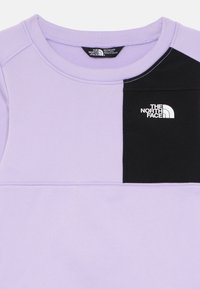 Jasnofioletowa bluza z czarnym panelem. Posiada białe logo The North Face na piersi, okrągły dekolt oraz miękką teksturowaną tkaninę.