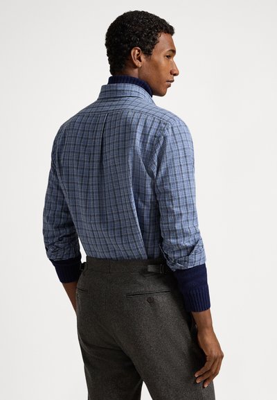 Mėlyna languota marškinėliai su aukštu apykakliu, kontrastingomis tamsiai mėlynomis rankogaliais ir nugaros klostėmis. Derinama su pilkais tekstūruotais kelnėmis.