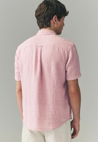 Pink majica kratkih rukava s teksturiranim materijalom. Leđa imaju središnji nabor i detalj s gumbom na ovratniku.