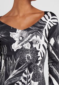 Svart bodysuit med vita blom- och lövtryck, med V-ringning och långa ärmar, tillverkad av ett slätt, elastiskt material.