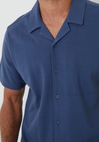 Kortemouwen shirt in een diepe blauwe kleur, met een gestructureerde stof, een kraag en vier bijpassende knopen aan de voorkant.