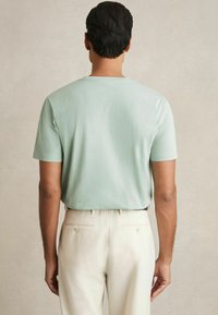 Tricou scurt de culoare verde mentă, cu o textură netedă, croială lejeră, asociat cu pantaloni eleganți de culoare crem, având buzunare la spate și nasturi.