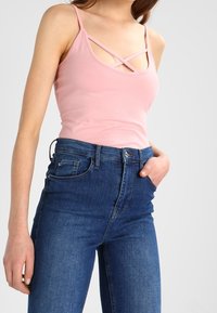 Ljusrosa linne med korslagda axelremmar, kombinerat med högmidjade mörkblå jeans i denim med klassisk femficksdesign.