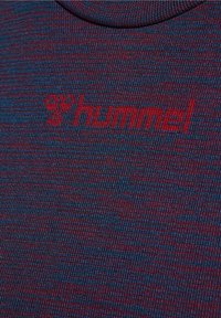 Lähedalt vaadatuna sinine ja tumepunane kootud kangas, millel on punane "hummel" logo ja mesilase embleem brodüüritud.