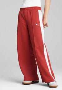 Røde atletiske bukser lavet af glat stof, med en hvid side-stribe, elastisk talje og en lynlåslomme.